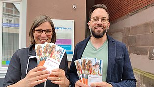 Zwei Personen zeigen Flyer in die Kamera
